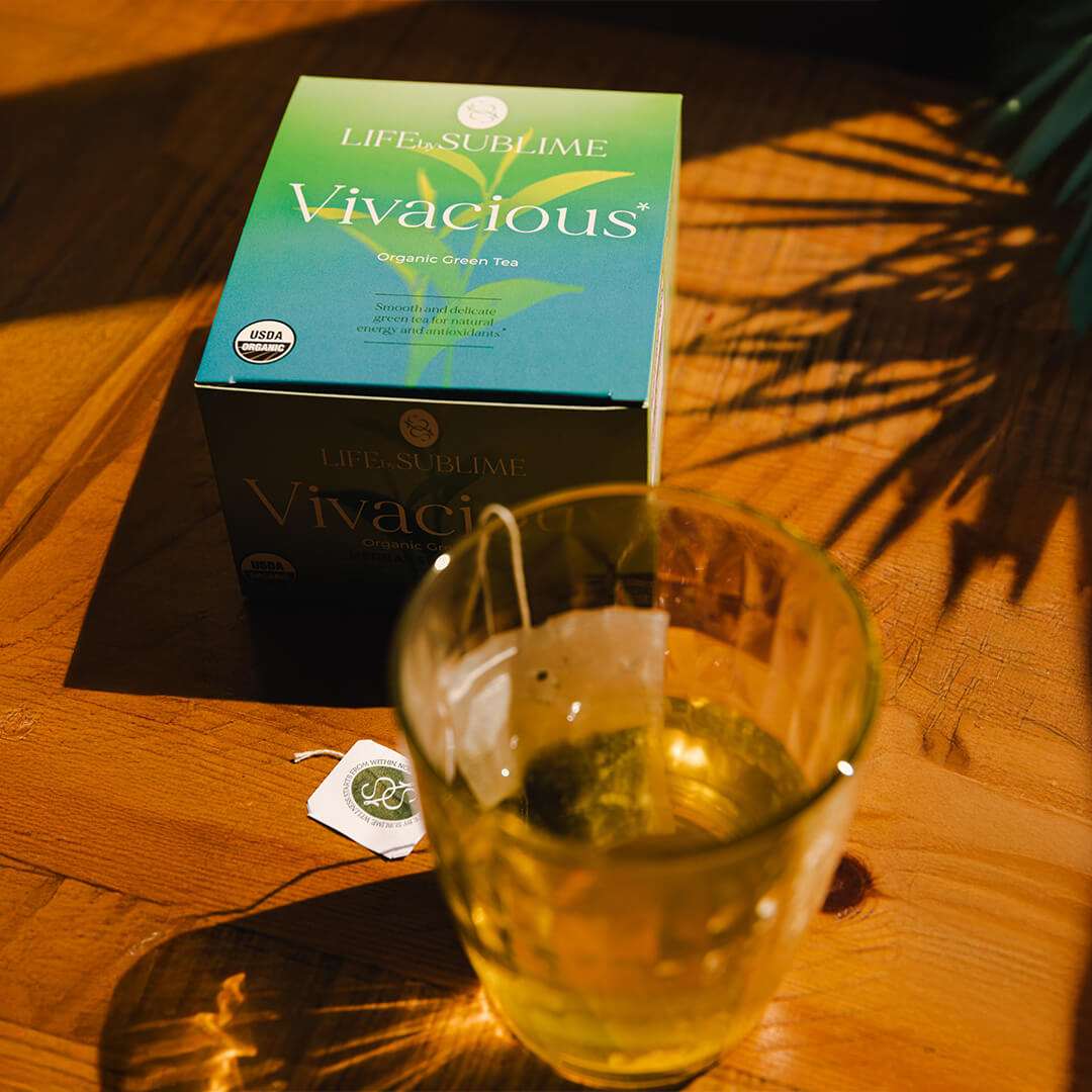 Vivacious organic green tea packaging next to glass of hot steeped fresh tea.