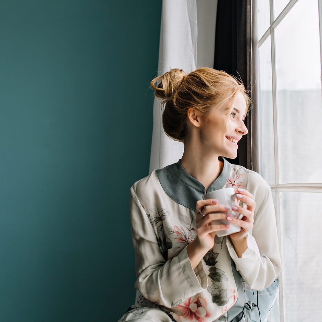 Woman enjoying life by sublime organic teas by the window.